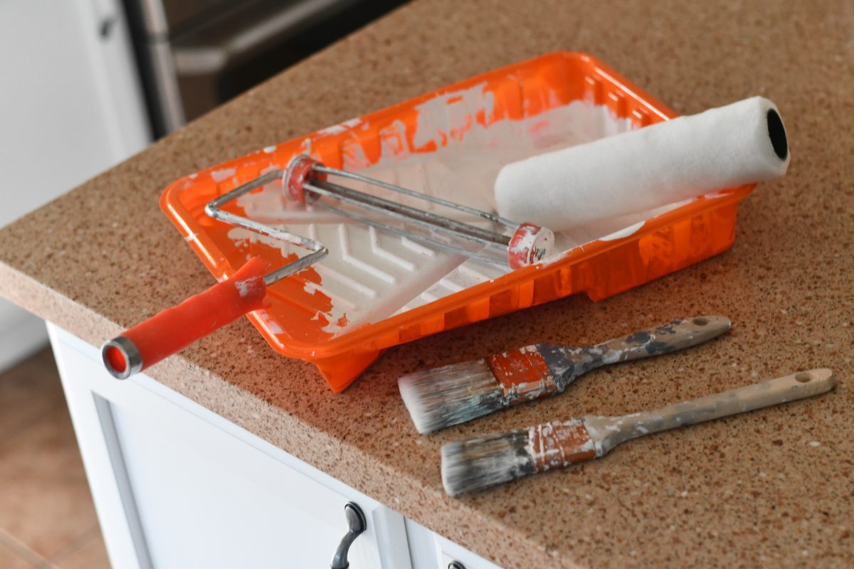 paint roller, cover, two paint brushes, and paint tray on a counter
