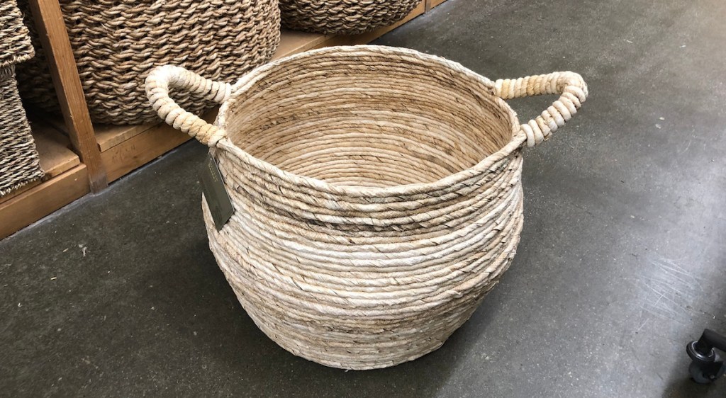 round natural woven basket with handles sitting on the floor