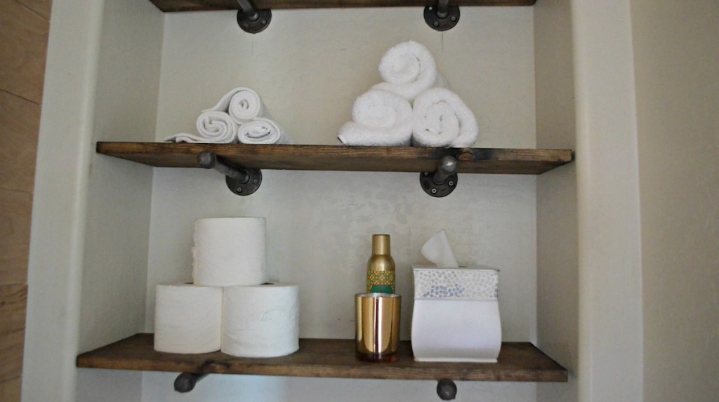 two brown and black wood shelves with toilet paper white towels and tissues