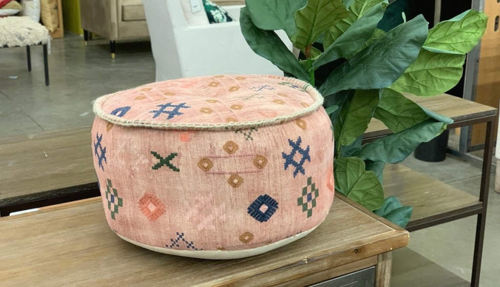 blush ottoman with abstract shapes and colors sitting on a table next to a plant 
