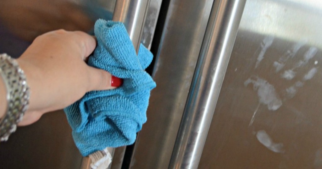 woman using microfiber cloth to clean stainless steel fridge
