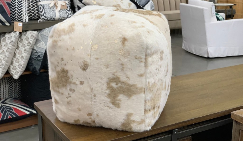 gold and white cowhide pouf foot stool sitting on top of a table