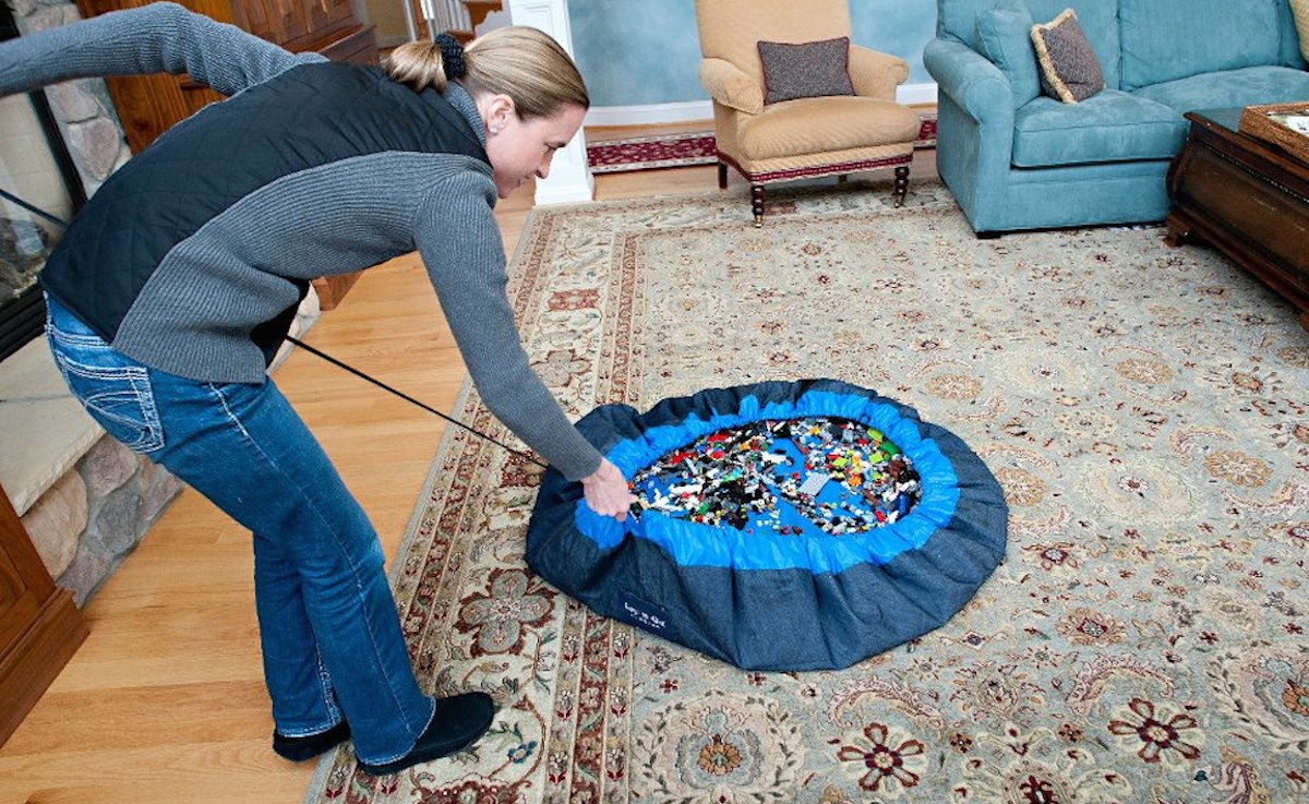 mom closing a blue drawstring bag with small legos inside of living family room