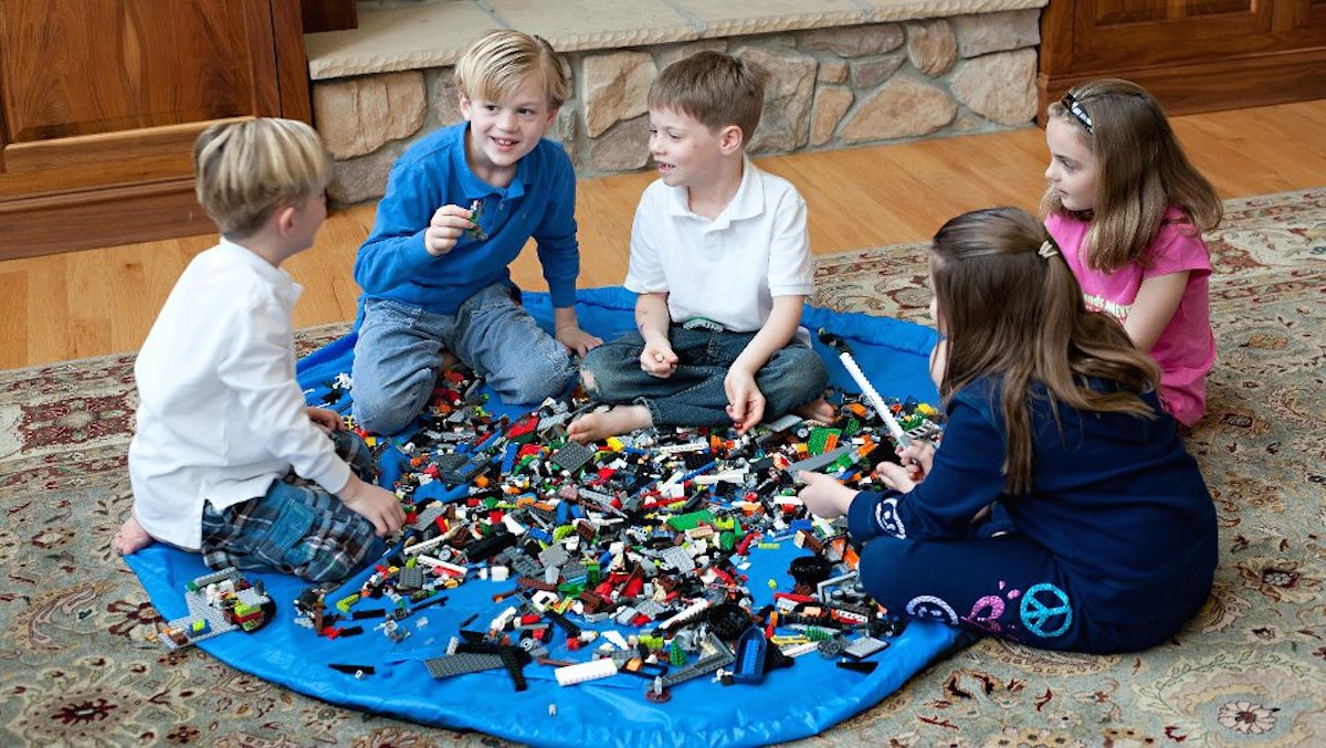 four kids playing on a blue at with legos