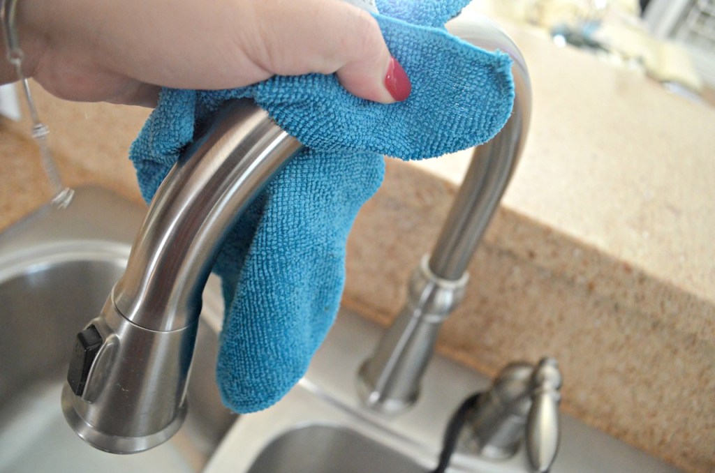 woman using microfiber cloth to clean stainless steel faucet