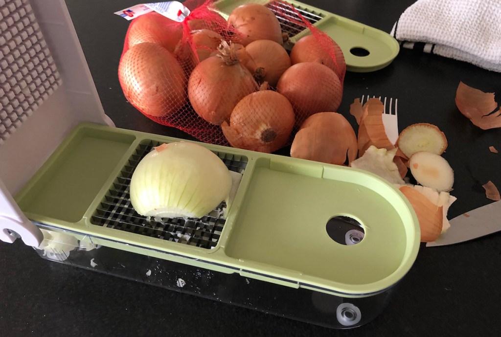 half onion sitting on sharp food chopper with bag of onions in the background