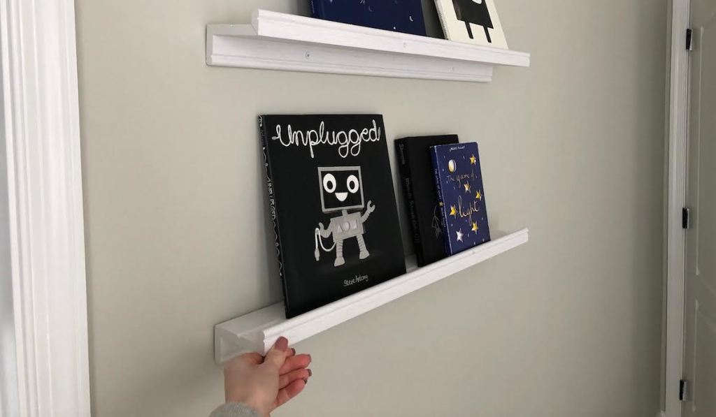 two white ikea floating shelves with books on them