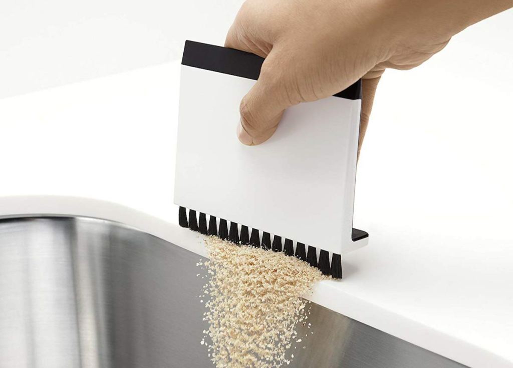 hand brushing crumbs off white countertop into sink