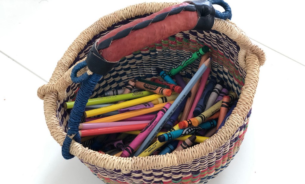 colorful market basket with leather handle on desk with colored pencils and crayons inside