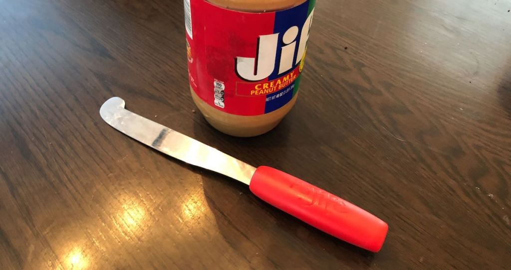 long red peanut butter spreader laying on counter with jar of jif peanut butter