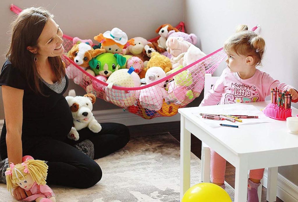 mom smiling at daughter with pink hammock in corner of room filled with stuffed animals
