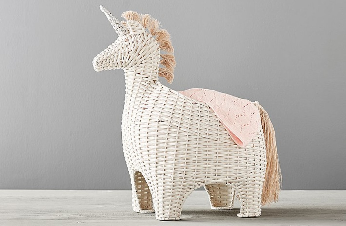 cream ivory unicorn wicker basket sitting on gray floor with blanket draped on the side