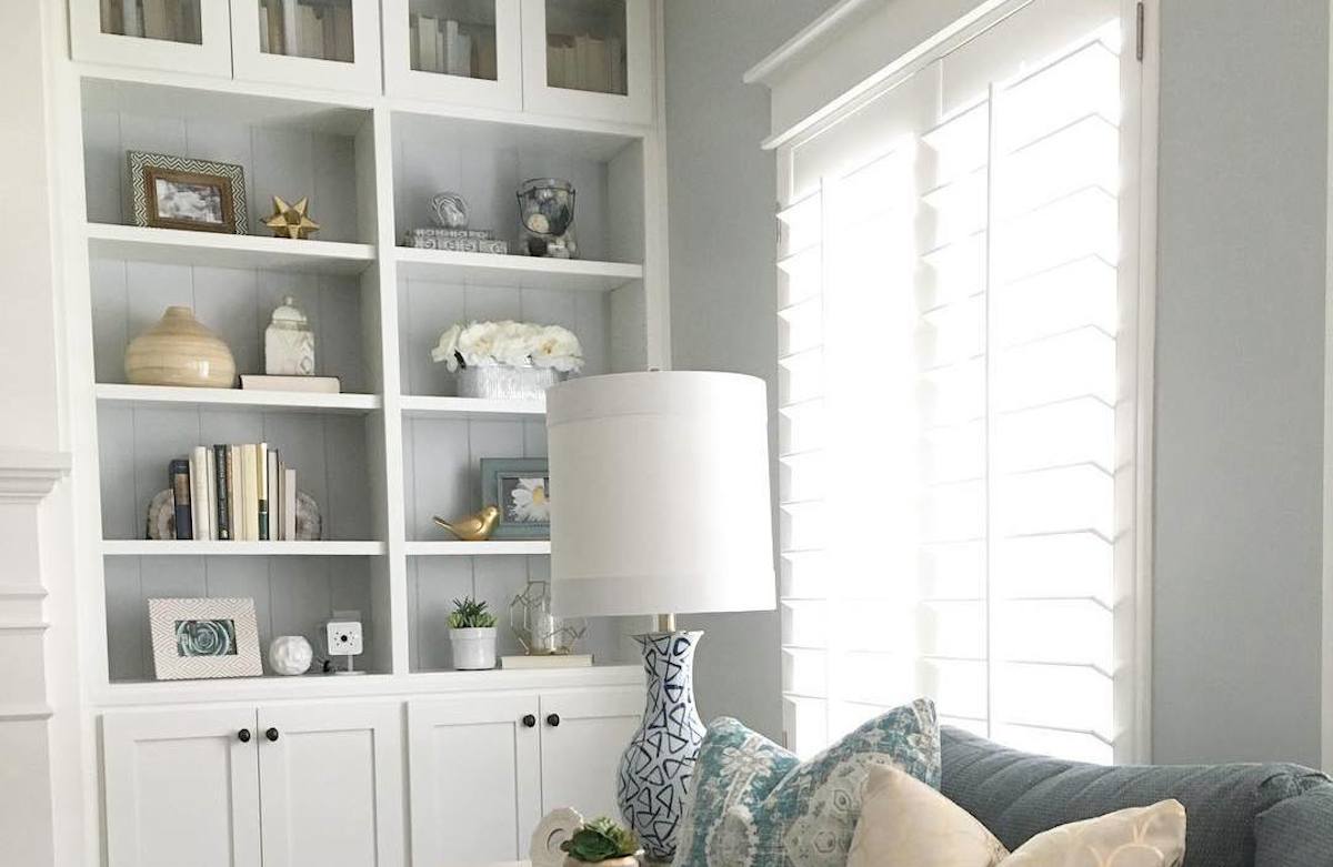 white bookshelves with decor and gray walls with a lamp and couch in front of window