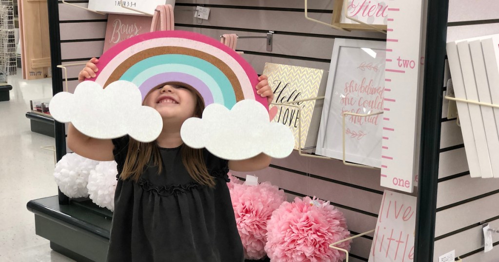 girl holding rainbow room decor in store aisle smiling