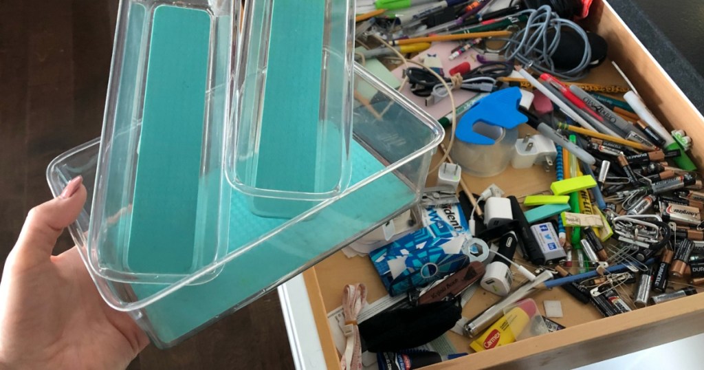 hand holding plastic organizers with messy junk drawer in the background