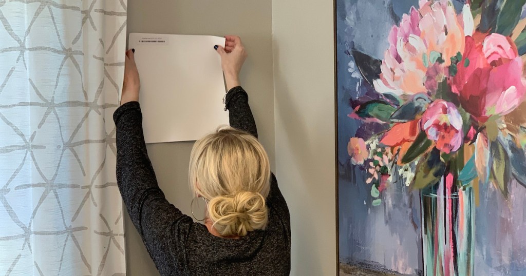 Collin holding a white square paint sample next to curtain and floral artwork