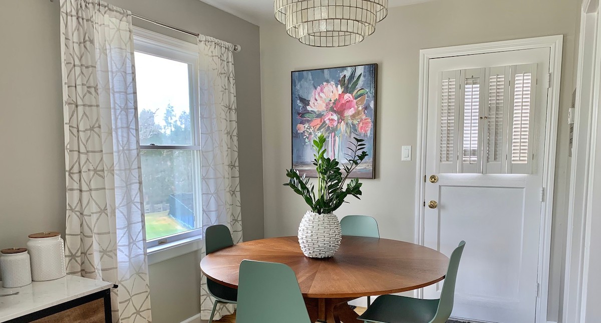 breakfast nook with floral artwork white curtains wood round table and blue green chairs