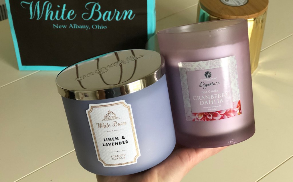 hand holding two purple floral scented candles with white barn bag in background
