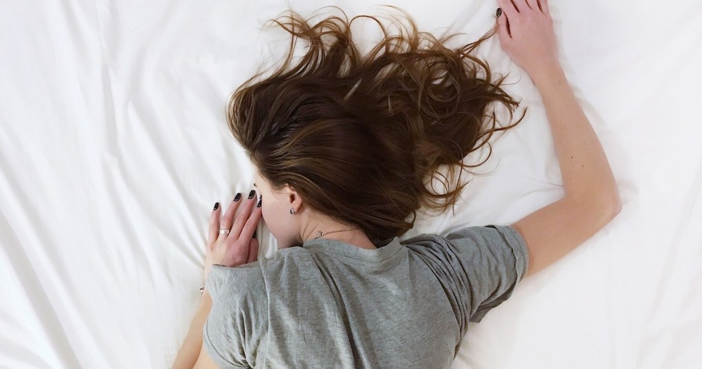 girl with brown hair laying on white sheets