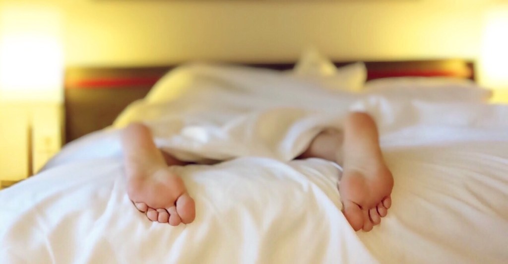 pair of feet hanging off white bed with bright yellow lights in background