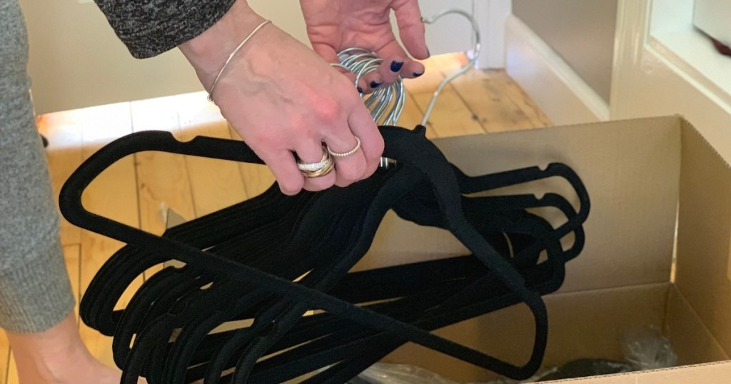 hands picking up pile of black velvet hangers from box