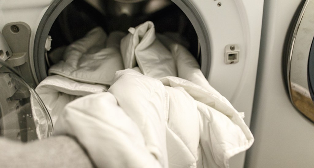 arm holding up white weighted blanket in front load washing machine