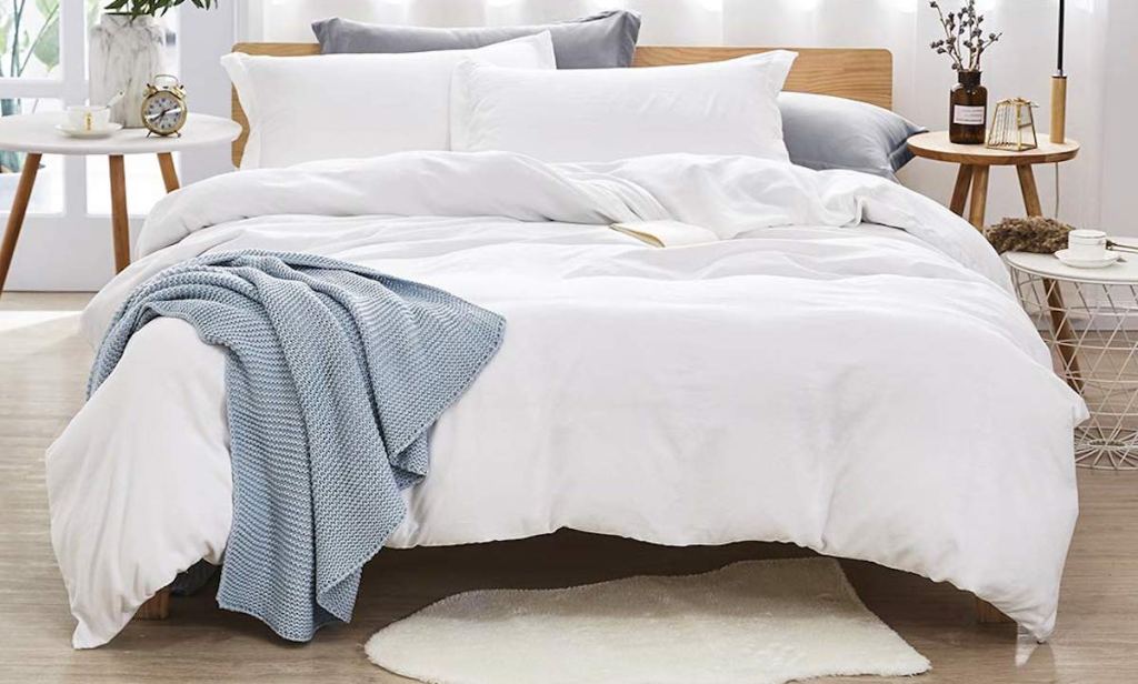 white bedding with pillows and blue throw with small white rug on floor