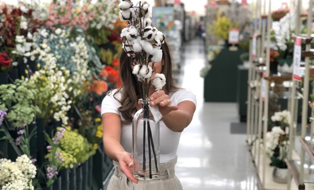 sara holding cotton stems in glass vase in floral aisle at store