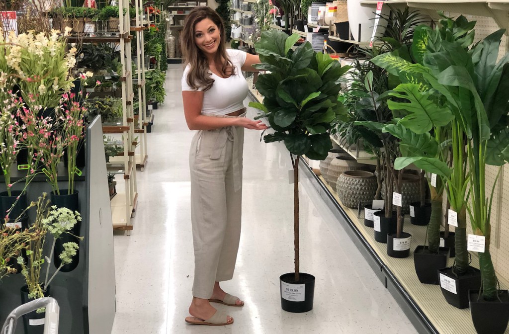 sara standing next to a tall fiddle leaf fig tree in store aisle