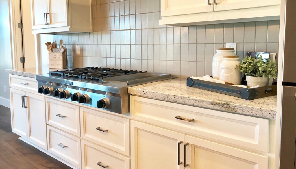 cream colored kitchen cabinets stainless steel range with black knobs and granite stone counters