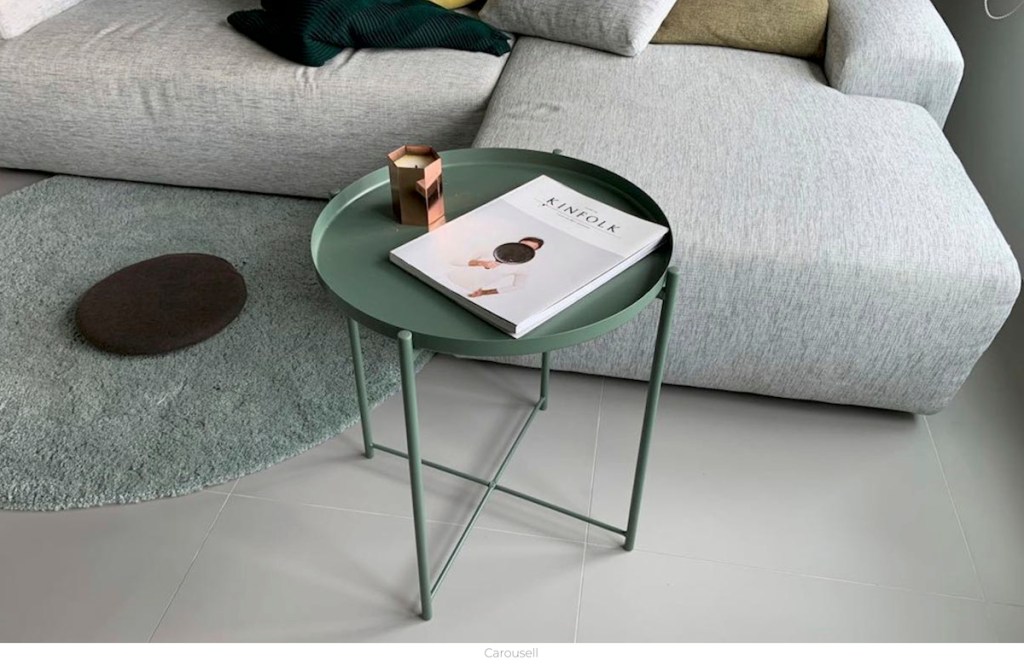 green side table with candle and magazine gray couch and rug in background