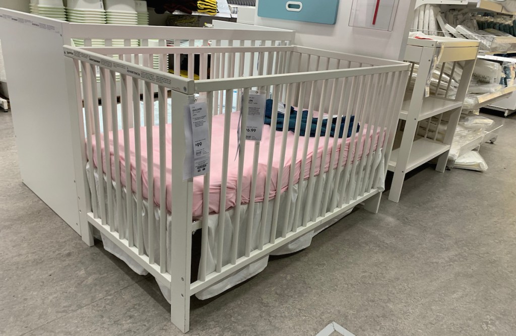 white crib with pink fitting sheet with price tags on front