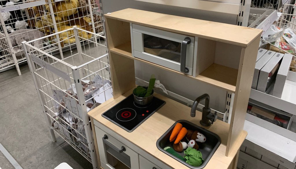 natural and white kids wooden kitchen in store with felt vegetables in sink