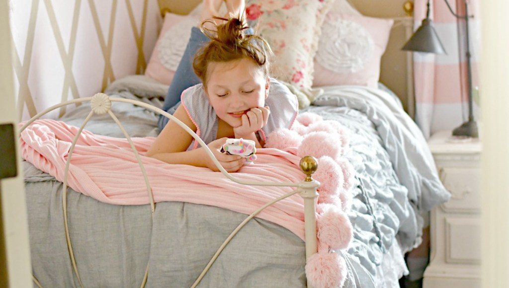 teen girl laying on bed with gray duvet and pink pom blanket