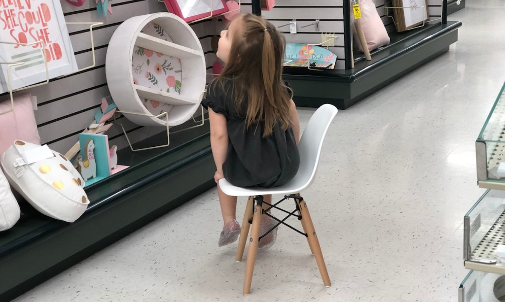 girl sitting on small modern white chair in store aisle