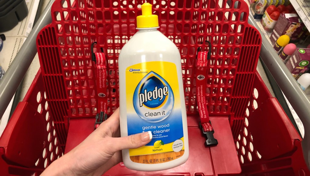 hand holding pledge floor cleaner bottle over a red target cart