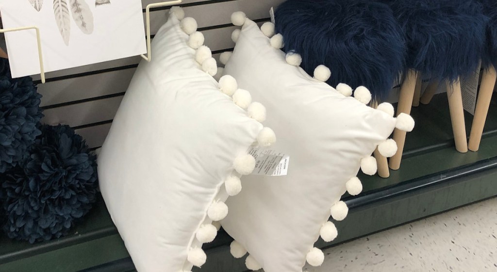 two white pom pillows sitting on shelf next to navy blue fur stools and decorative paper balls
