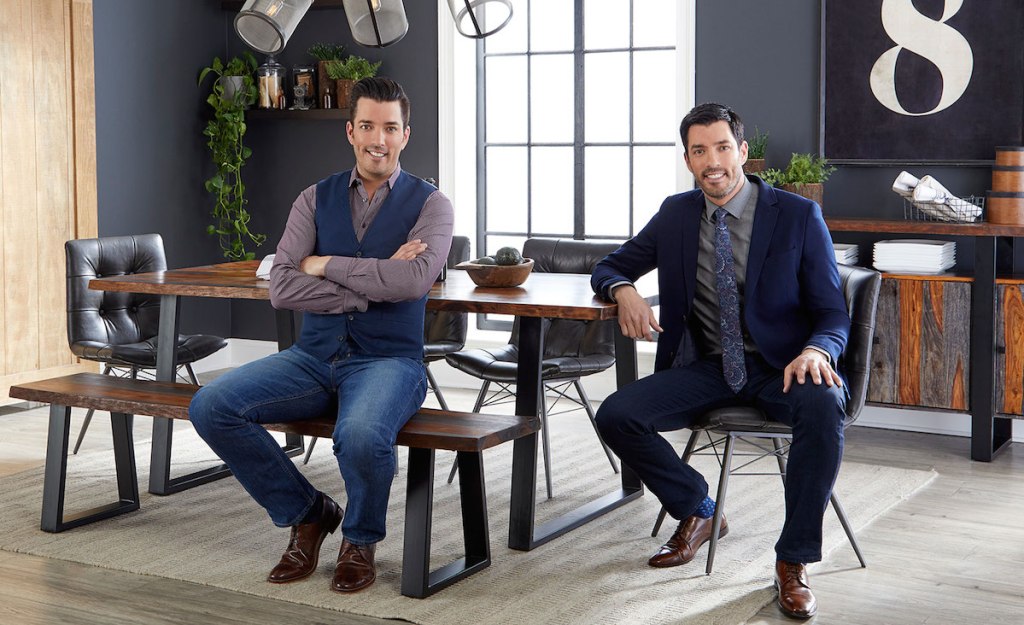 drew and johnathan scott dressed in suits sitting at wood dining table set