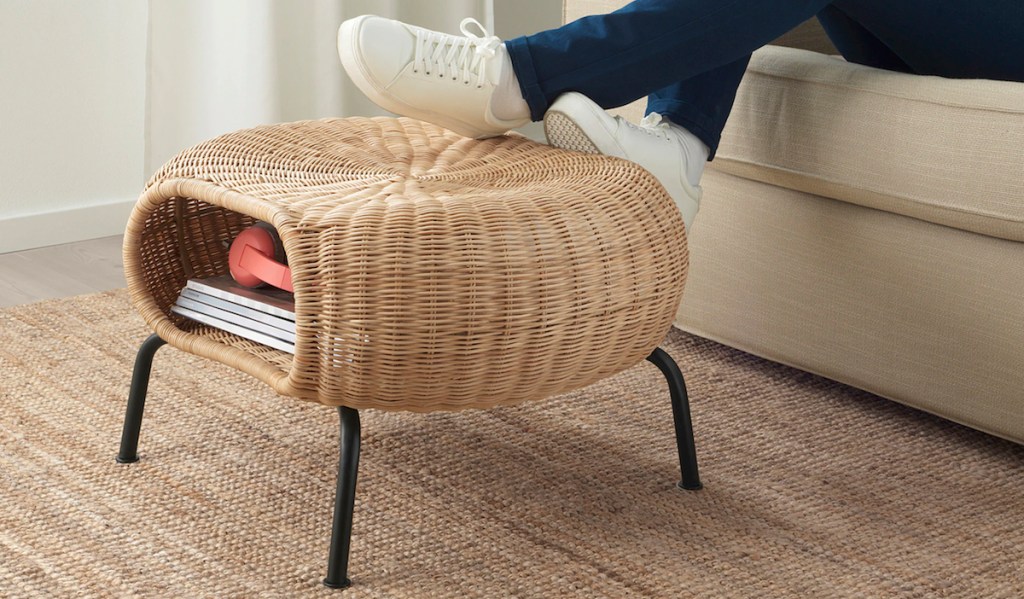 feet resting on round wicker ottoman with black legs and books inside