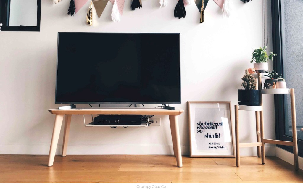 tv on wood stand with banner above it on the wall and picture frame on wood floor