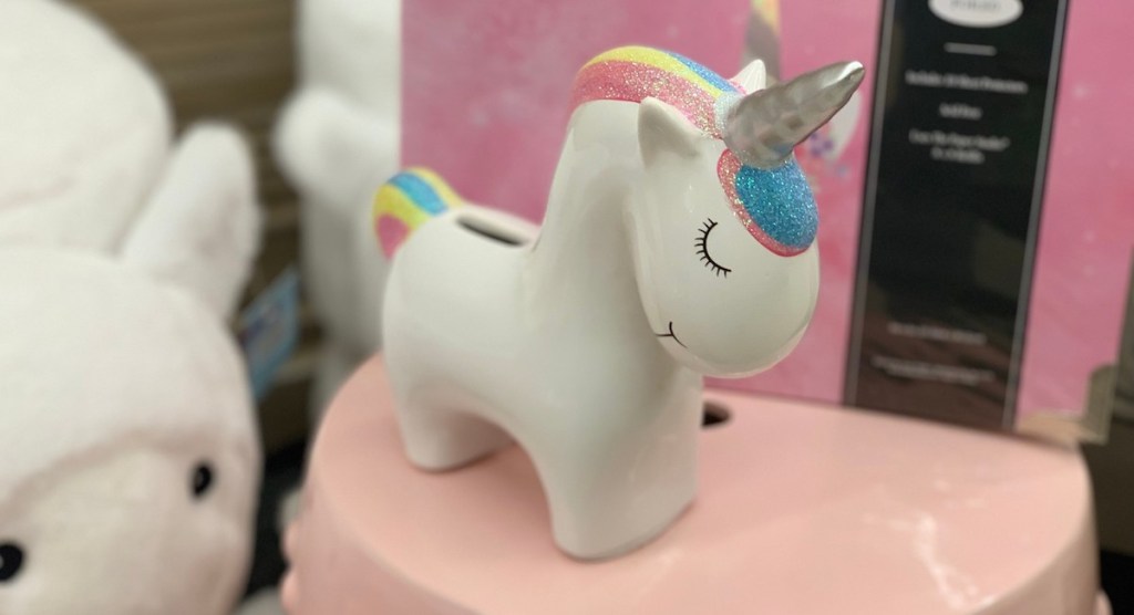 white glass ceramic unicorn piggy bank with rainbow hair standing on pink table