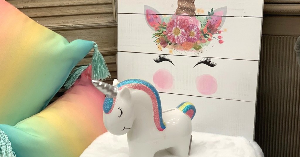 glass ceramic white unicorn bank with rainbow hair next to rainbow tassel pillows and artwork