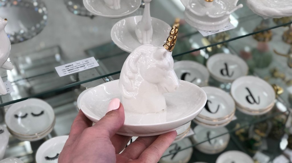 hand holding a white unicorn ring holder with glass items in background