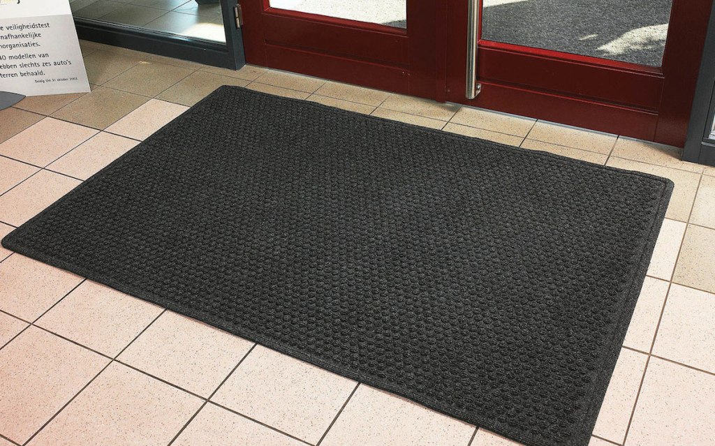 black door mat sitting on beige tile floor