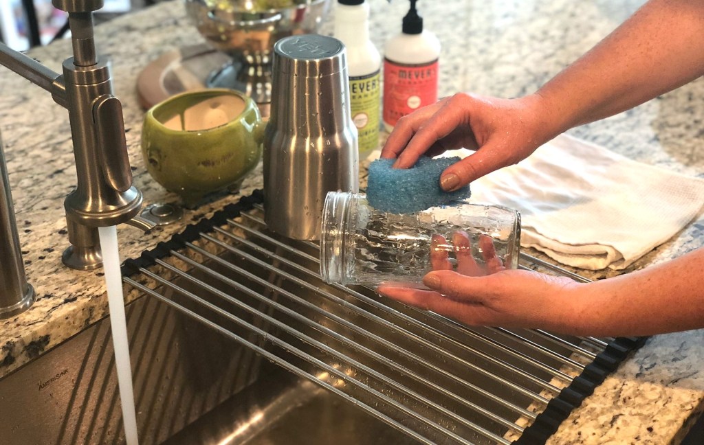 hand washing a clear glass cup with running sink water