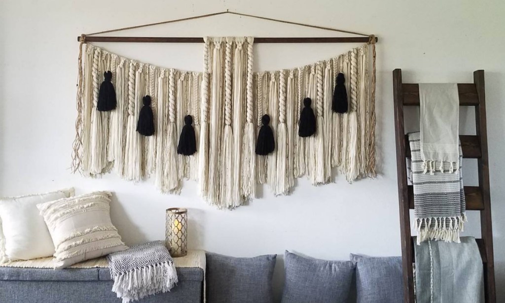 black and cream wall hanging on white wall gray couch with pillows and ladder on wall