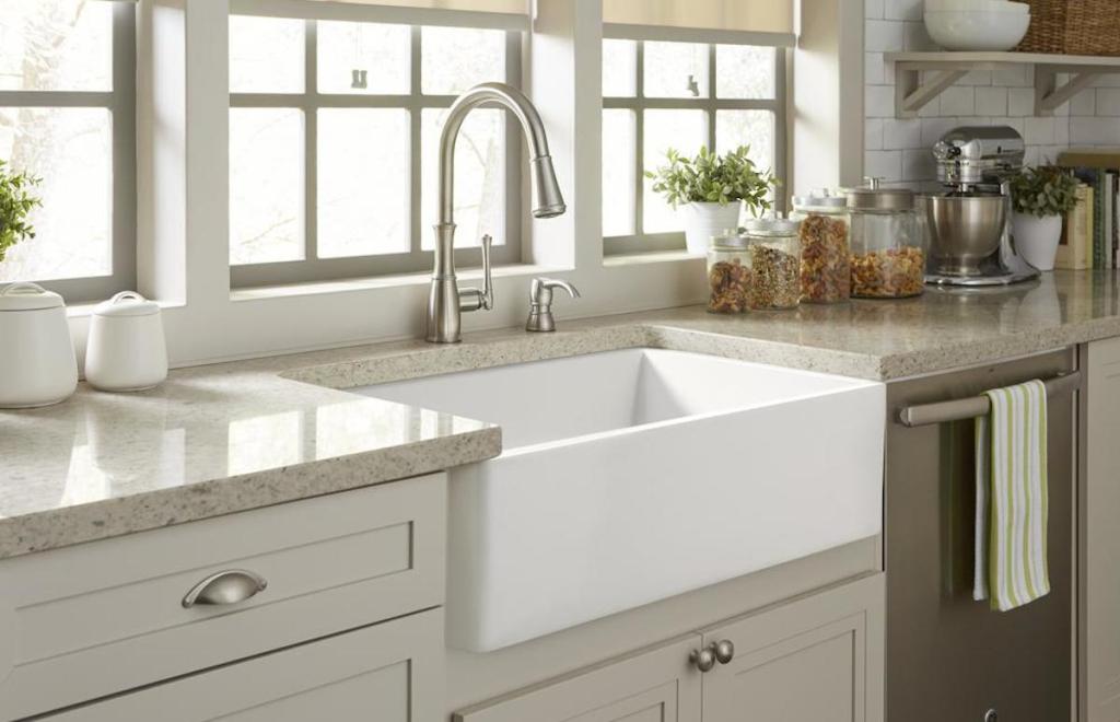 white apron sink with stainless steel faucet cream gray cabinets and stone countertops below large window