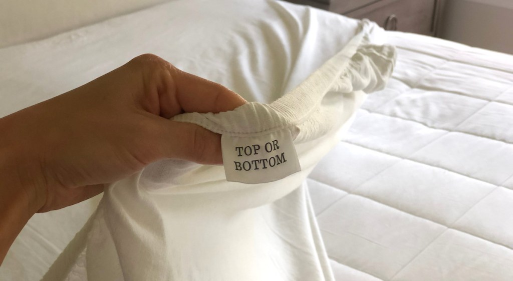 hand holding fitted sheet with top bottom tag on white sheets 