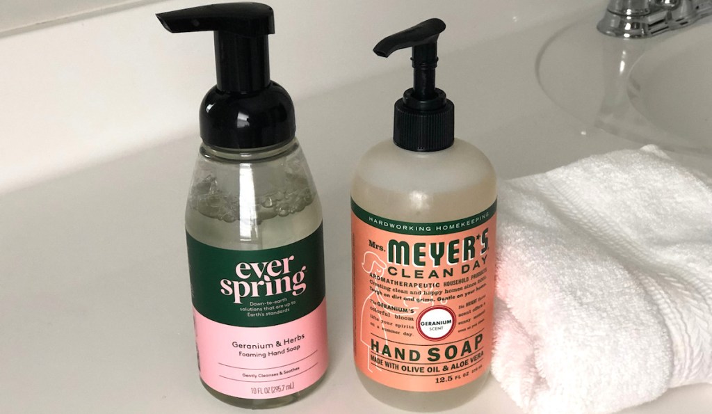 everspring pink geranium soap next to orange mrs meyers bottle with white towel on white countertop