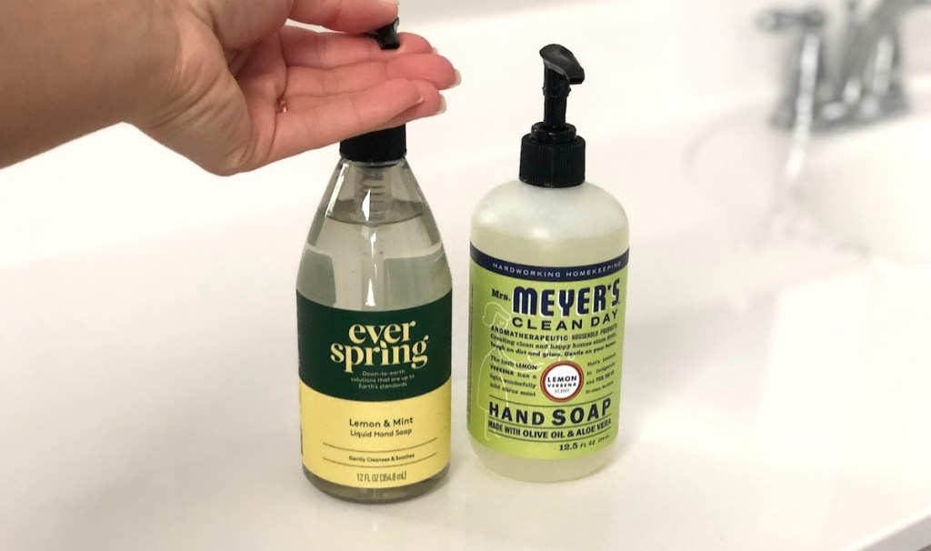 hand pushing down on everspring lemon hand soap next to green mrs meyers bottle
